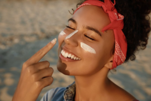 Woman smiling at the beach as she applies sunscreen to her face